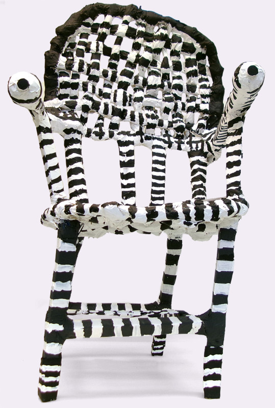 A fanciful chair sculpture painted with black and white stripes. The pommels of the arm rests look like eyeballs. The seat back is woven. The entire thing is a little off-kilter.